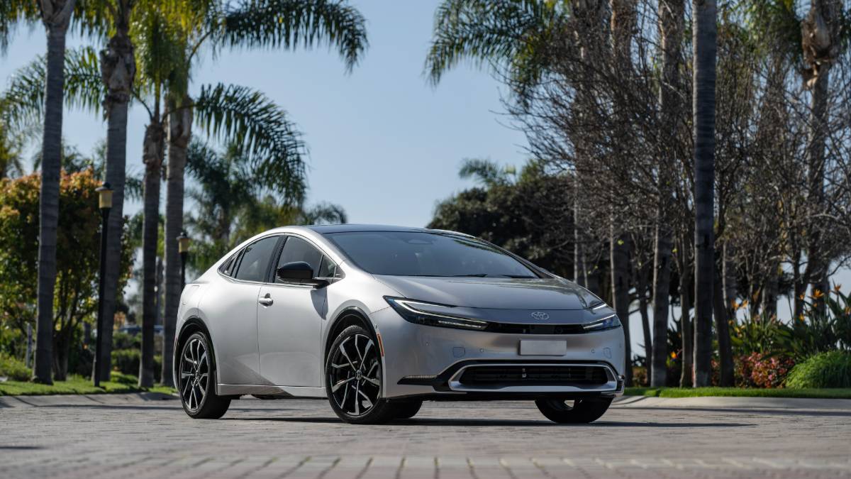 2025 Toyota Prius in silver parked on a palm tree-lined street, front three-quarter view showcasing sleek LED headlights and aerodynamic hybrid design.